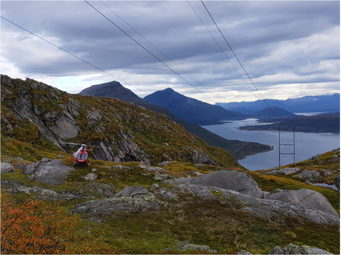 Illustrasjon av helikopter på toppen av et fjell med fjord i bakgrunnen