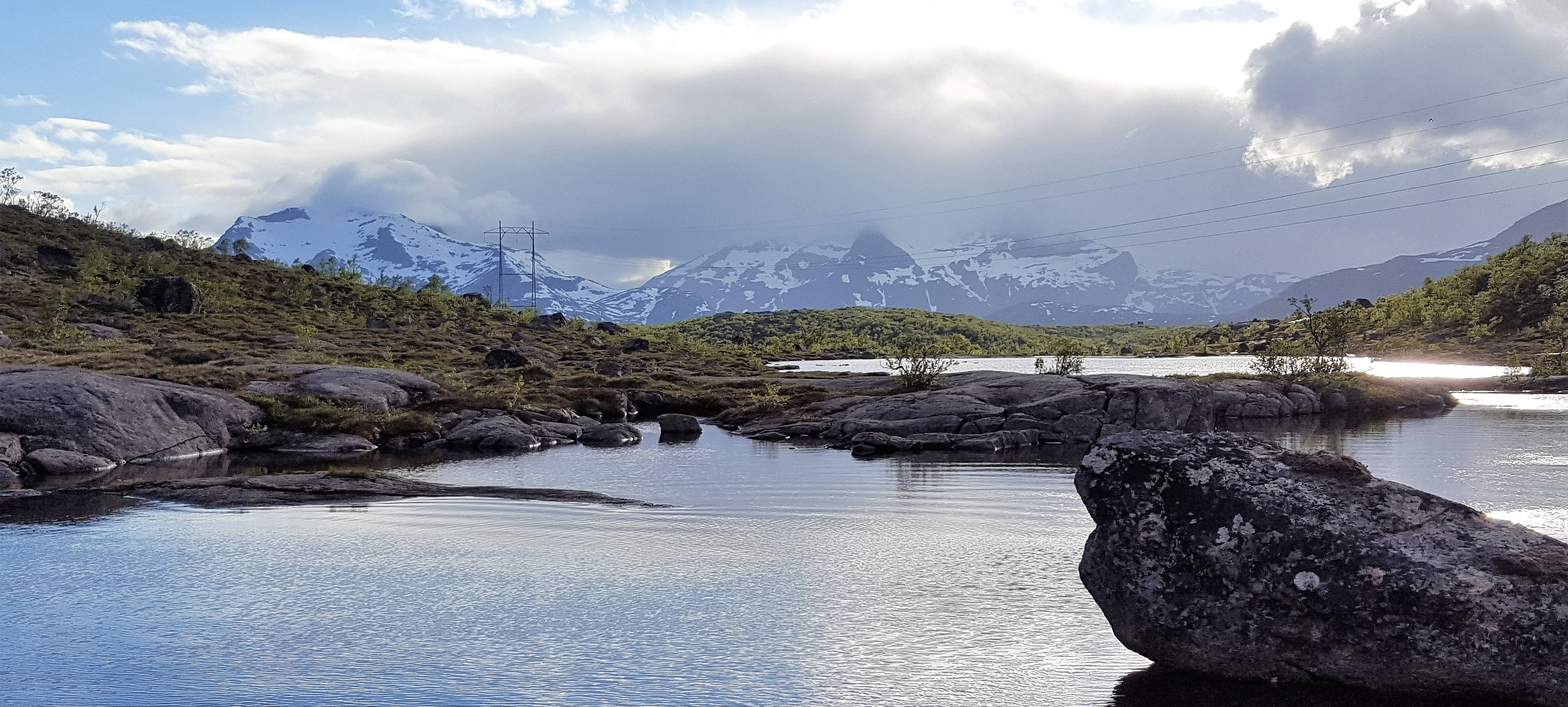 Strømmaster ved et vann med fjell og skog rundt 